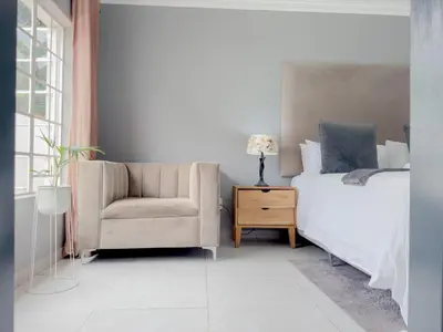a bedroom with a bed and a chair at Amoris Guesthouse - Hillcrest Brooklyn in Pretoria