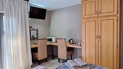 a room with a desk with chairs and a kitchen at Dormio Manor Guest Lodge in Secunda