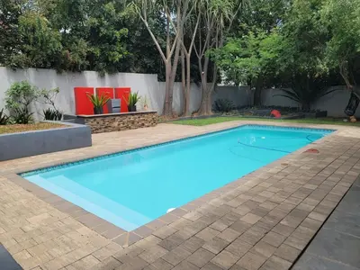 a blue swimming pool in a yard with trees at The Cottage in Secured Estate in Pretoria
