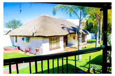 a house with a thatched roof with a balcony at Fairy Gardens Lodge in Pretoria