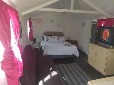 a bedroom with a bed with pink curtains and a tv at Chalet 5 At Cynthias Country in Hartbeespoort