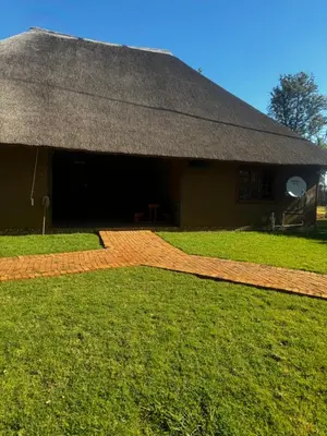 a building with a thatched roof and a grass field at Falcon Lodge Bela in Bela-Bela