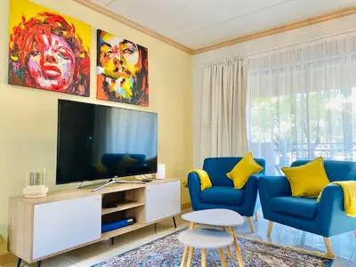 a living room with two blue chairs and a television at Phoenix Rising Apartment in Midrand