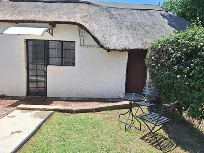 a small house with a thatched roof with a table in front at Midrand-Living Water's Sanctuary in Midrand