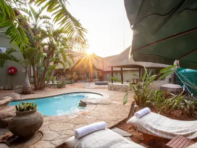 a swimming pool with two lounge chairs and a house at Etnika Manor House in Hoedspruit