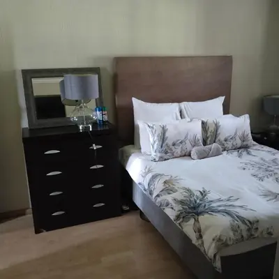 a bedroom with a bed with a dresser and a mirror at Melkbos Place in Witbank