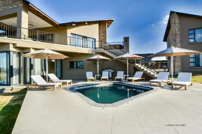 a patio with a pool and chairs and umbrellas at Zebula Golf Estate & Spa Executive Holiday Homes in Mabula