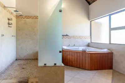 a bathroom with a tub and a shower with a window at Zebula Golf Estate & Spa Executive Holiday Homes in Mabula
