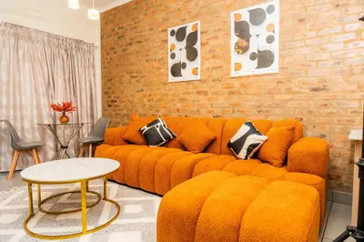 a living room with an orange couch and a brick wall at Palm Nest in Kempton Park