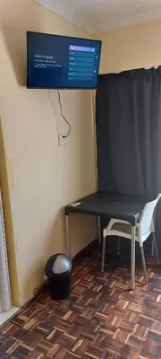 a table and a chair in a room with a screen at Rest at 54 Gladiator Guesthouse in Kempton Park
