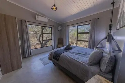 a bedroom with a bed and two large windows at Chui House A Bush Retreat with Pool and AC Near Kruger Gate in Marloth Park