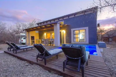 a house with a deck with chairs and a swimming pool at Chui House A Bush Retreat with Pool and AC Near Kruger Gate in Marloth Park