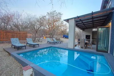 a swimming pool in a yard with chairs and a patio at Chui House A Bush Retreat with Pool and AC Near Kruger Gate in Marloth Park