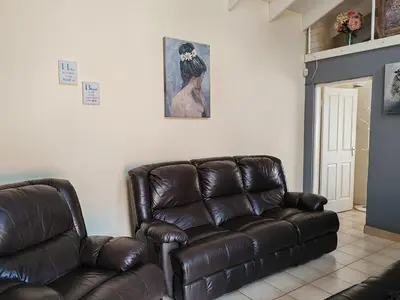 a living room with a brown leather couch and a painting at Skuinslê in Centurion