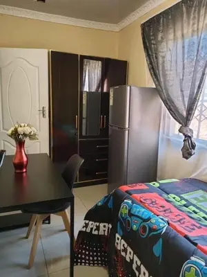 a bedroom with a bed and a table and a refrigerator at Siba's Place in Ga-Rankuwa