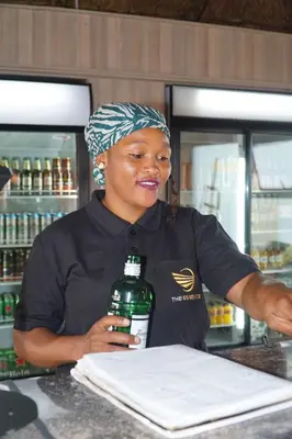 a woman standing behind a counter holding a bottle of alcohol at The Essence Resort in Clarence
