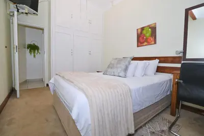 a bedroom with a bed with white sheets and a chair at The Hellens Guest House in Pretoria