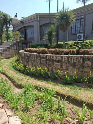 a house with a retaining wall and yellow flowers at Aaybee Recreational Home in Midrand