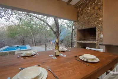 a wooden table with plates and a bottle of wine at The Bush House Kruger in Marloth Park