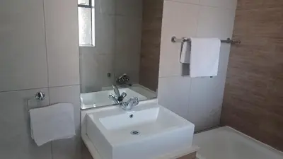 a white bathroom with a sink and a mirror at Generous Apartment at Waterfall in Midrand