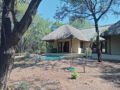 a house with a thatch roof and a swimming pool at Iphupho Bush Lodge, Ba-Phalaborwa Golf Estate in Phalaborwa
