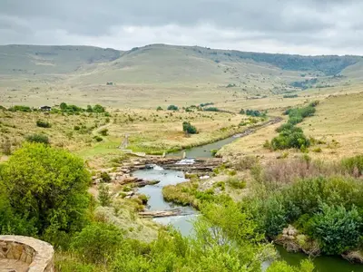 a river in a field with mountains in the background at Riverbend on Komati in Machadodorp
