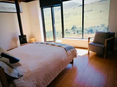 a bedroom with a bed and a chair and windows at Riverbend on Komati in Machadodorp