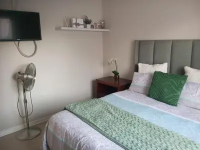 a bedroom with a bed with a green blanket and a fan at Simply Stay in Polokwane