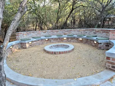 a brick fire pit with green benches in a yard at Warthog's Retreat in Marloth Park