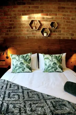 a bedroom with a white bed with a brick wall at Warthog's Retreat in Marloth Park