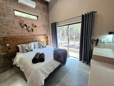 a bedroom with a bed and a brick wall at Warthog's Retreat in Marloth Park