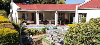 a white house with a table and chairs in the yard at Faerie Glen B&B in Pretoria