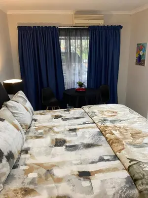 a bedroom with a large bed with blue curtains at Cozy Garden Flat with Garden in Pretoria