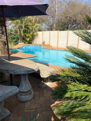 a swimming pool with an umbrella and a table with at Cozy Garden Flat with Garden in Pretoria