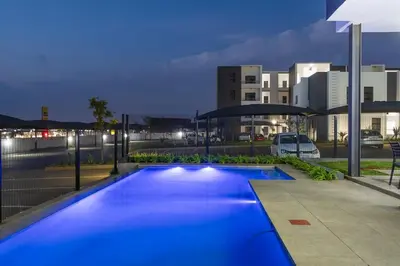 a blue swimming pool in a city at night at Infinite Views Penthouse in Midrand