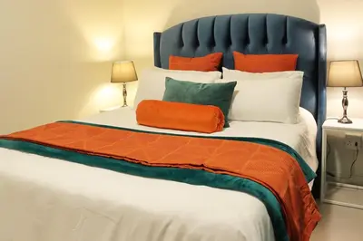 a large bed with an orange pillow on it at Infinite Views Penthouse in Midrand
