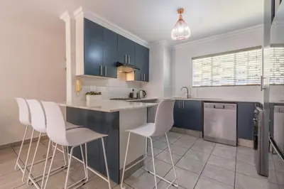a kitchen with blue cabinets and white stools at Menlyn Chique Apartment in Pretoria