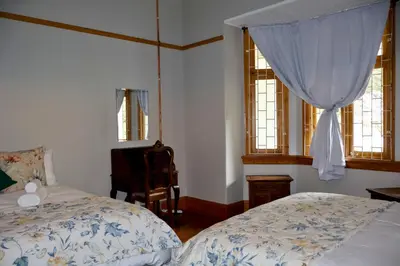 a bedroom with two beds and a chair and windows at The Dullstroom Inn in Dullstroom
