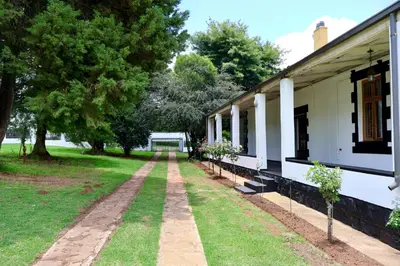 a walkway next to a white building with trees at The Dullstroom Inn in Dullstroom