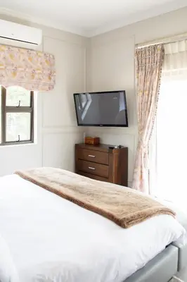 a bedroom with a bed and a flat screen tv at The African Penguin Guesthouse in Pretoria