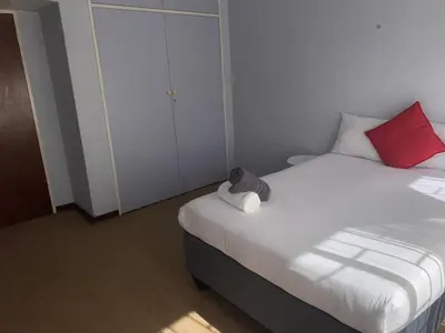 a small bedroom with a bed with white sheets and red pillows at Lynnwood 246 House in Pretoria