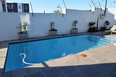 a blue swimming pool with a white wall at Eirini Elegant Hades Apartment in Midrand