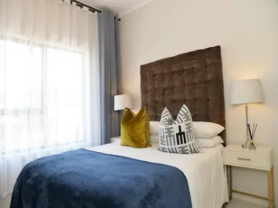 a bedroom with a bed with a blue blanket and yellow pillows at Eirini Elegant Hades Apartment in Midrand