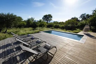 a deck with chairs and a swimming pool at Villa Blaaskans in Hoedspruit