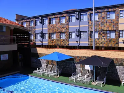 a pool with chairs and umbrellas in front of a hotel at The Empire Hotel in Vendaland