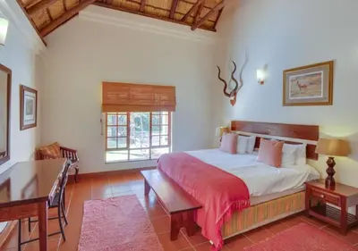 a bedroom with a bed and a table and a desk at Zebula 1 Pela Lodge, 4-bedroom house in Warmbaths