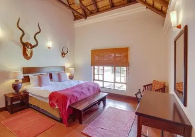 a bedroom with a bed and a desk and a window at Zebula 1 Pela Lodge, 4-bedroom house in Warmbaths