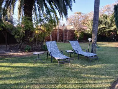 three chairs and a table in a yard with palm trees at Aero Ensuites- OR Tambo in Kempton Park