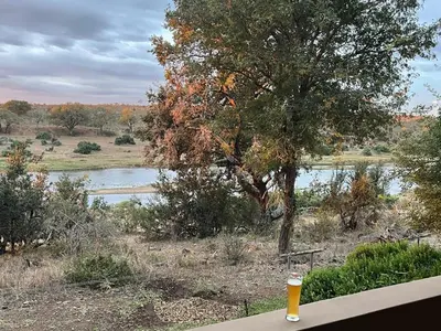 a glass of beer sitting on a table next to a river at Imberbe Private Lodge in Hectorspruit