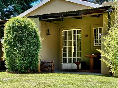 a small yellow house with a door and a bush at Stonefly Cottages in Dullstroom